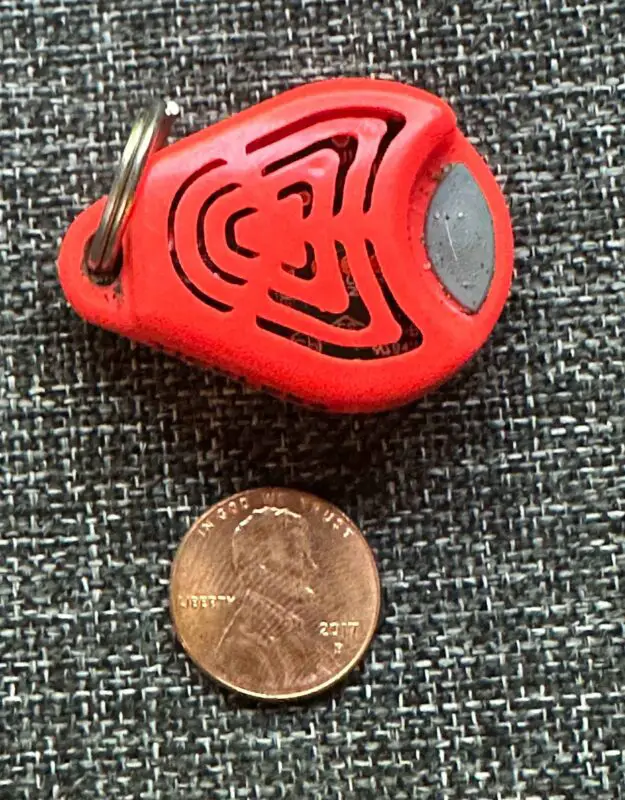 a orange Tickless Ultrasonic Flea & Tick Repellant next to a penny to show its small size